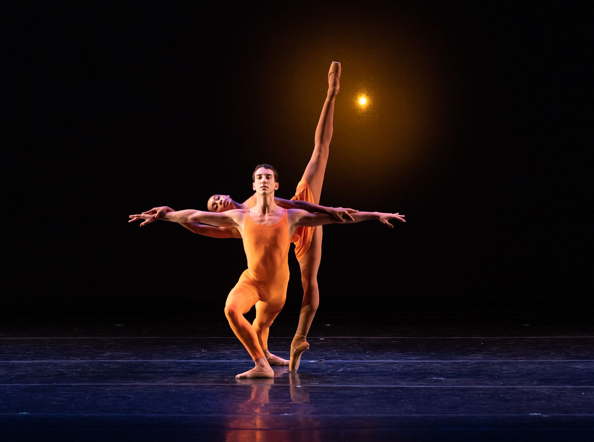 Two ballet dancers in red and black costumes pose in a dramatic stage performance