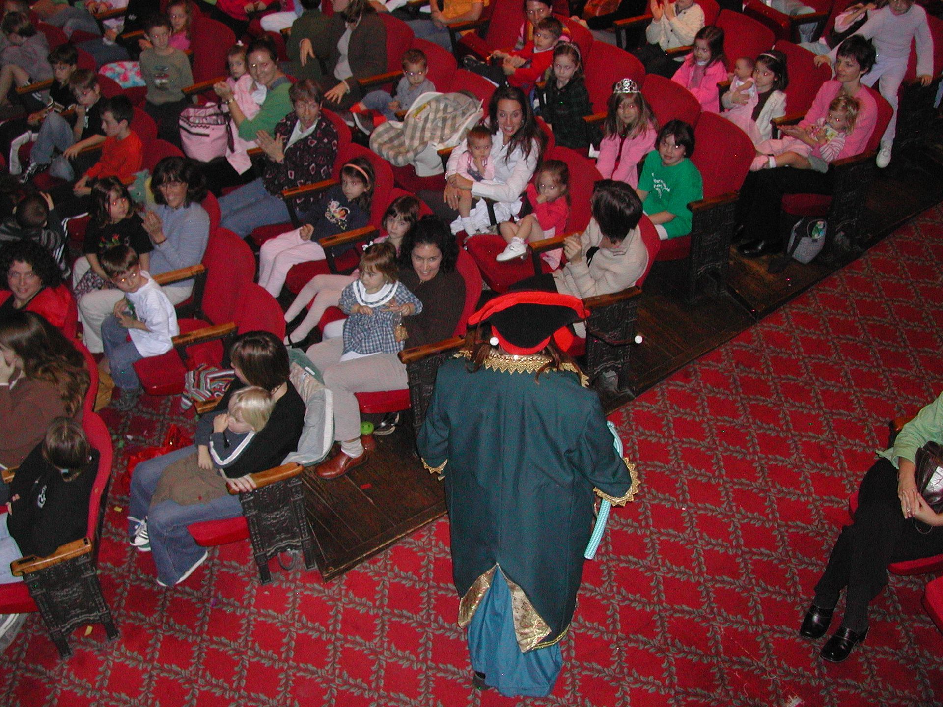 Audience seated in red theater chairs, viewed from above, with one person walking down the aisle