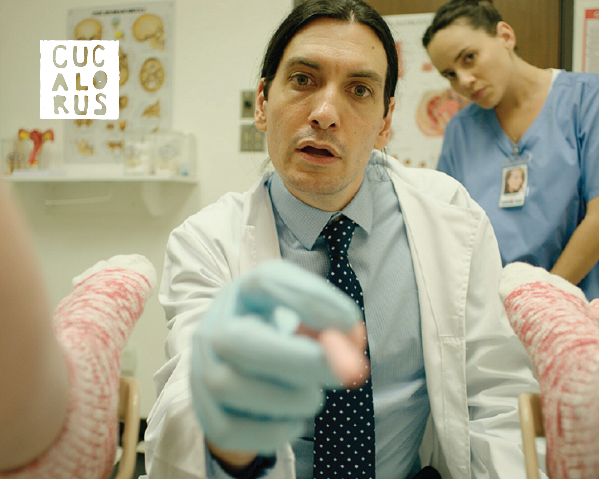 Doctor in lab coat points toward camera in a clinical room, with a nurse behind him and a CUCALORUS sign.