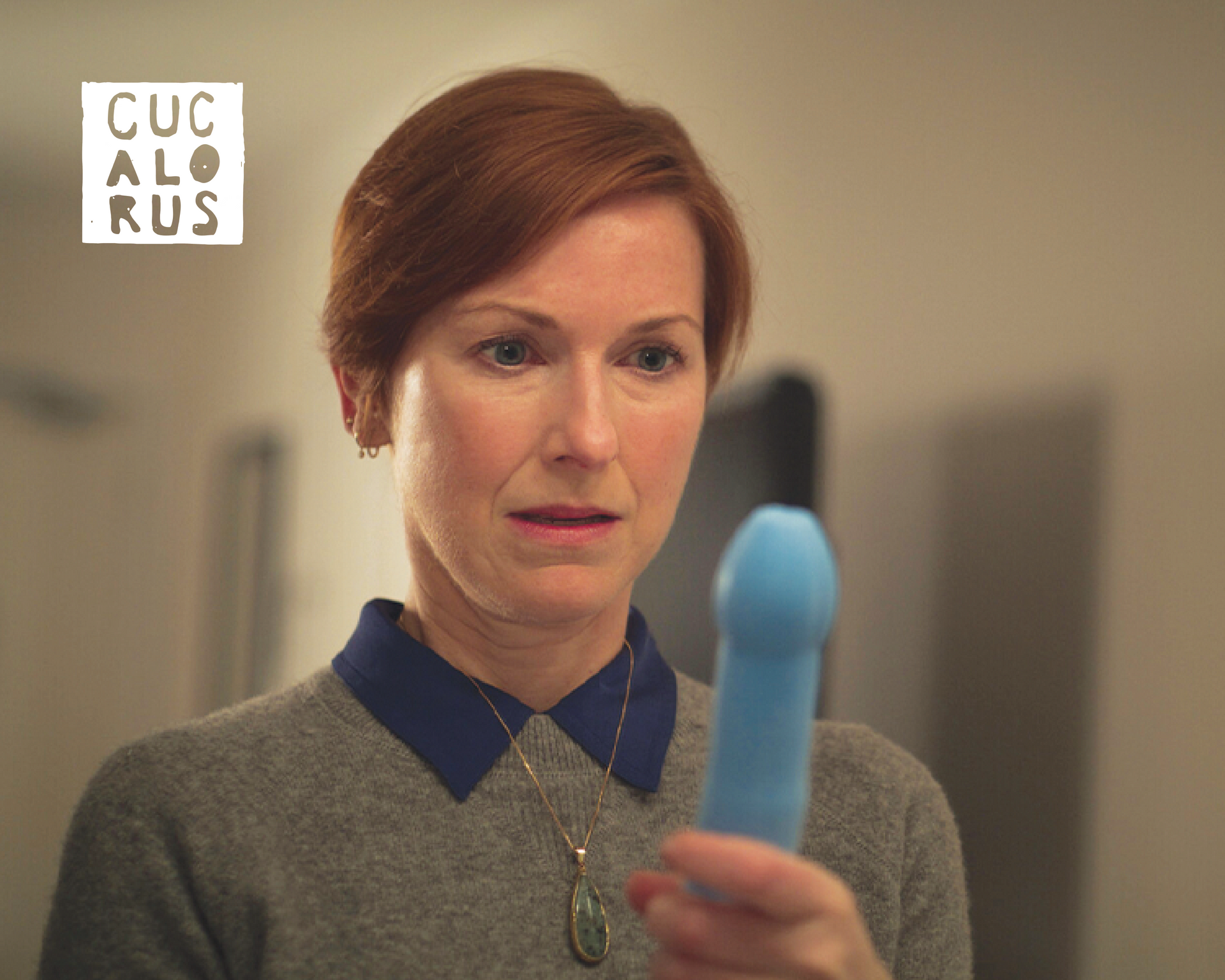 Woman in gray sweater holds a blue object, looking puzzled in a softly lit room