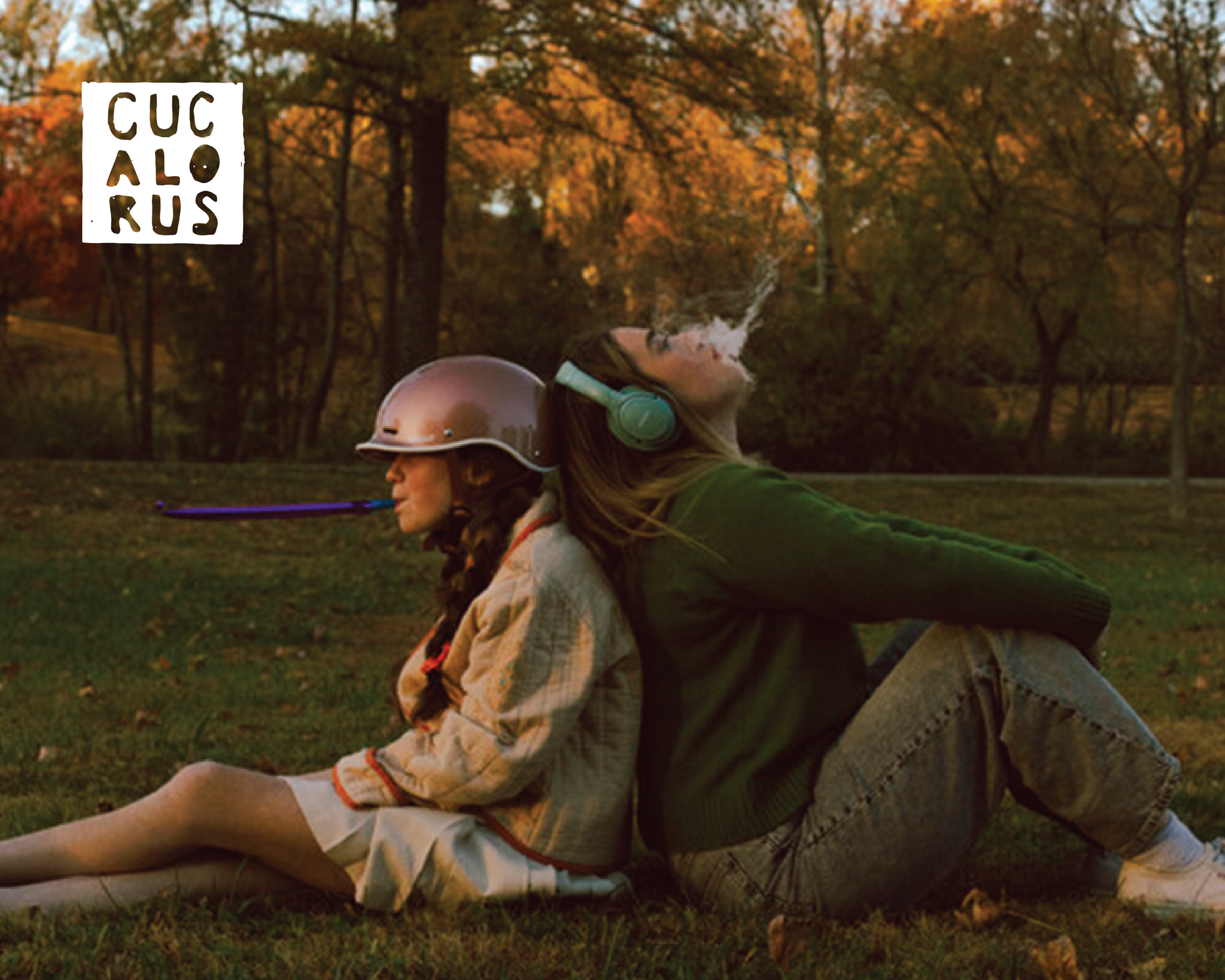 Two costumed people reclining on grass in a park at sunset, one wearing a helmet and long purple sword.
