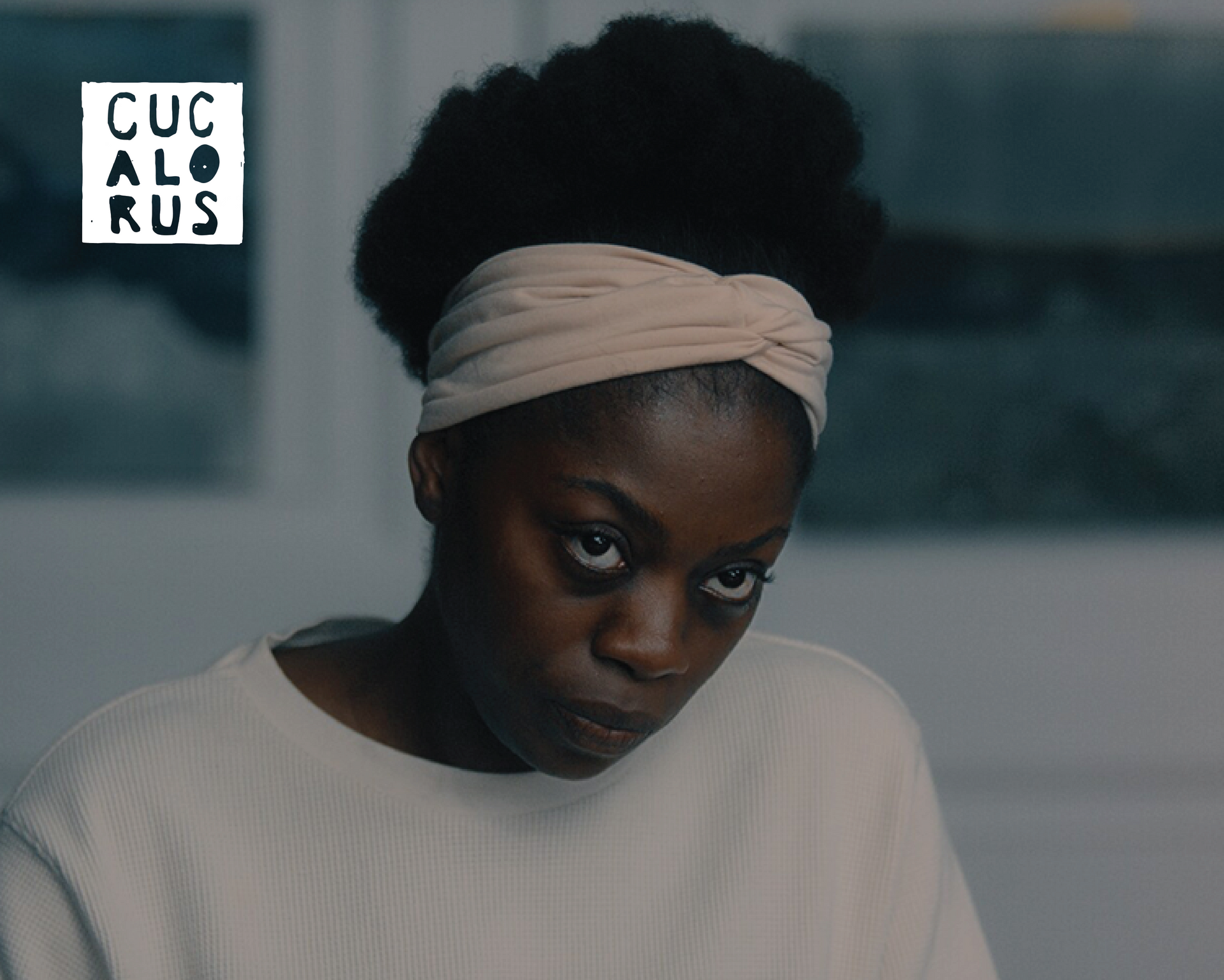 Woman in a white top and headwrap looking downward in a softly lit room, with a CUCALOS logo in the corner