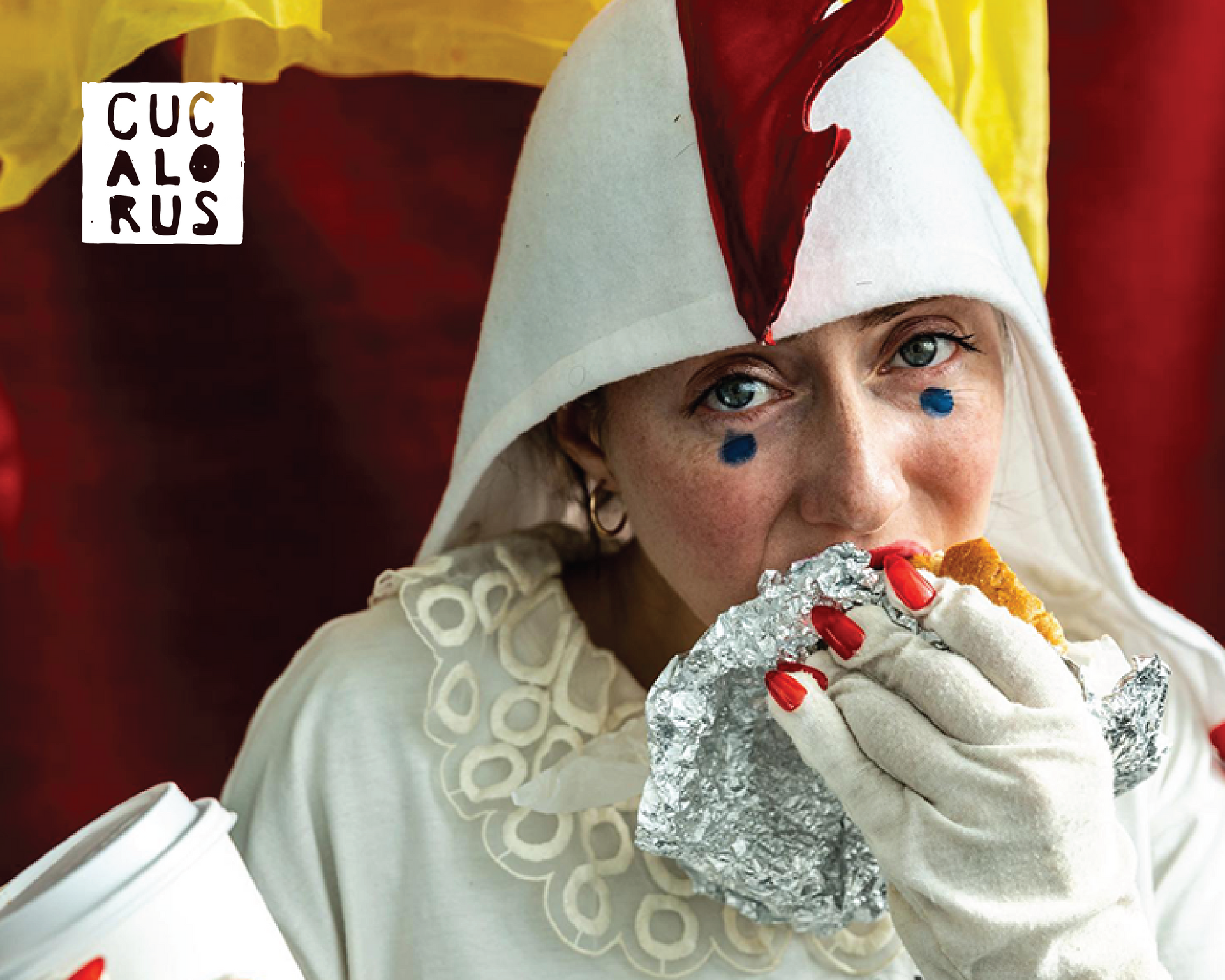 Person in a white hooded outfit eats a foil-wrapped sandwich, with blue teardrops painted on their face.
