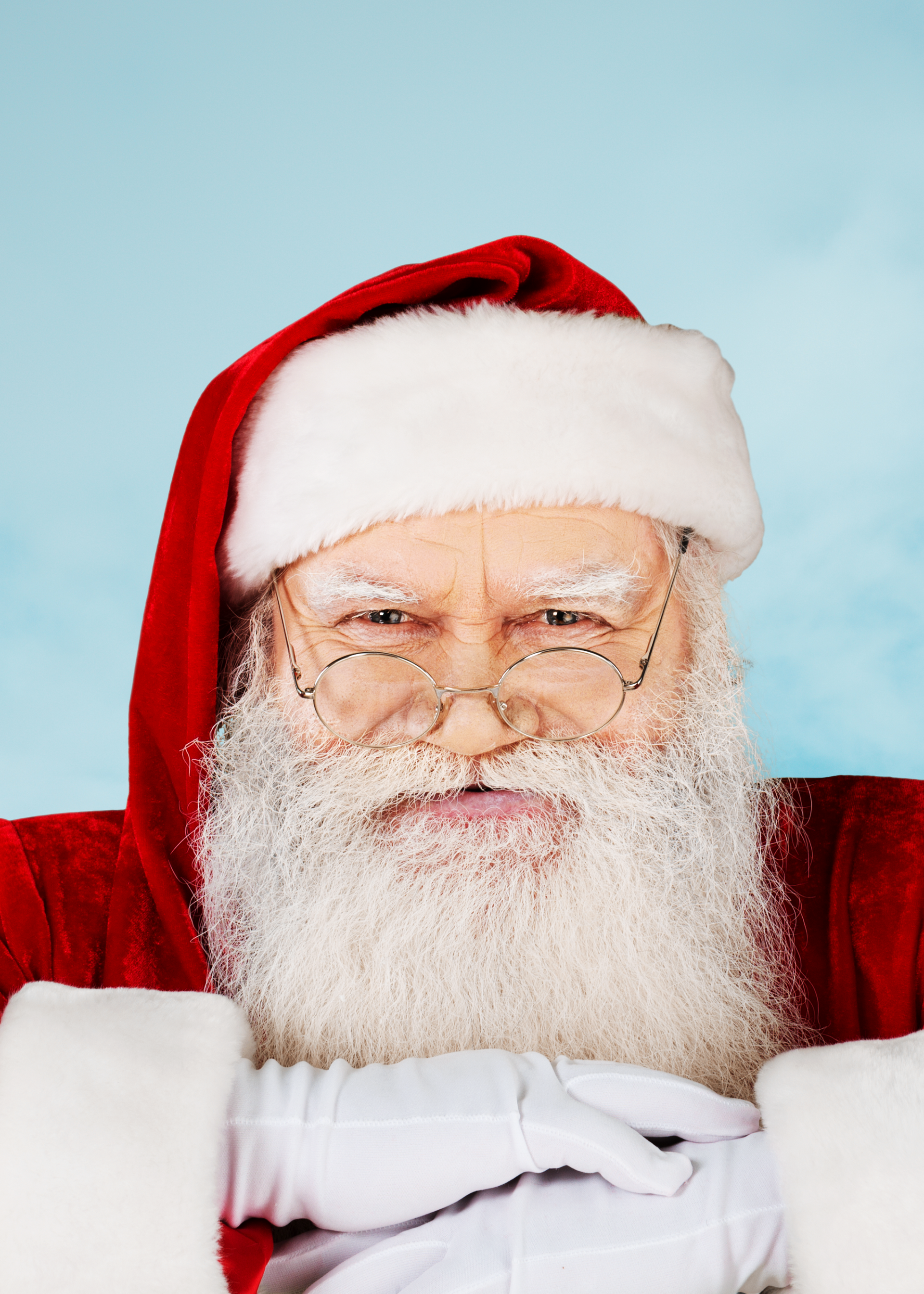 Santa in a red hat and coat against a light blue background, smiling with a white beard