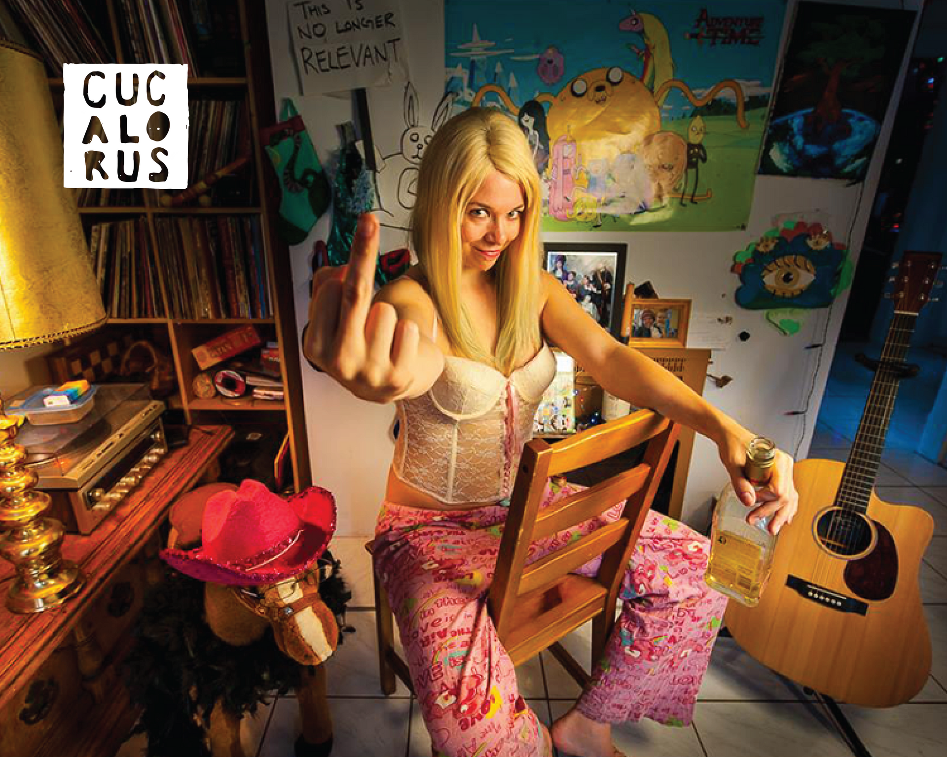 Blonde woman in a colorful bedroom strums guitar, with art-covered walls and a wicker chair nearby