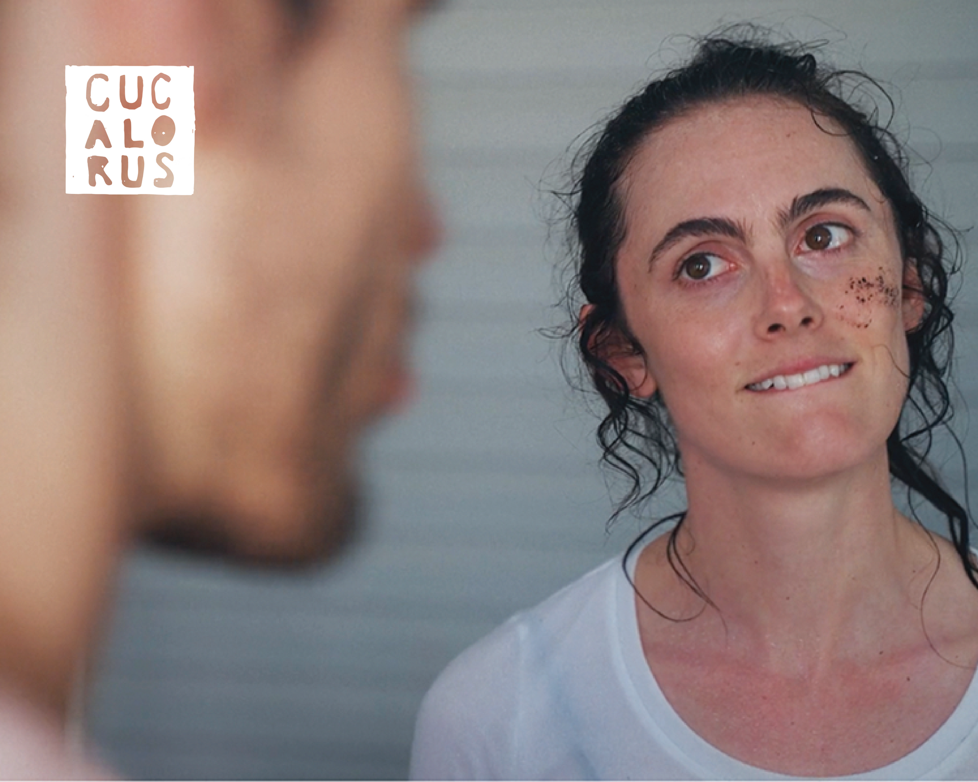 Woman with a slight smile faces a blurred person indoors, with a small CUCALORUS logo in the corner