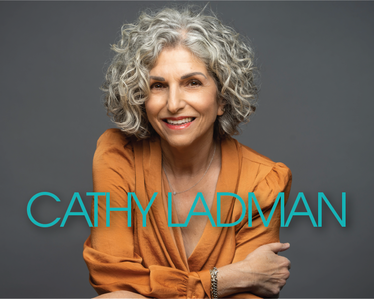 Portrait of Cathy Ladman smiling in an orange top against a gray background
