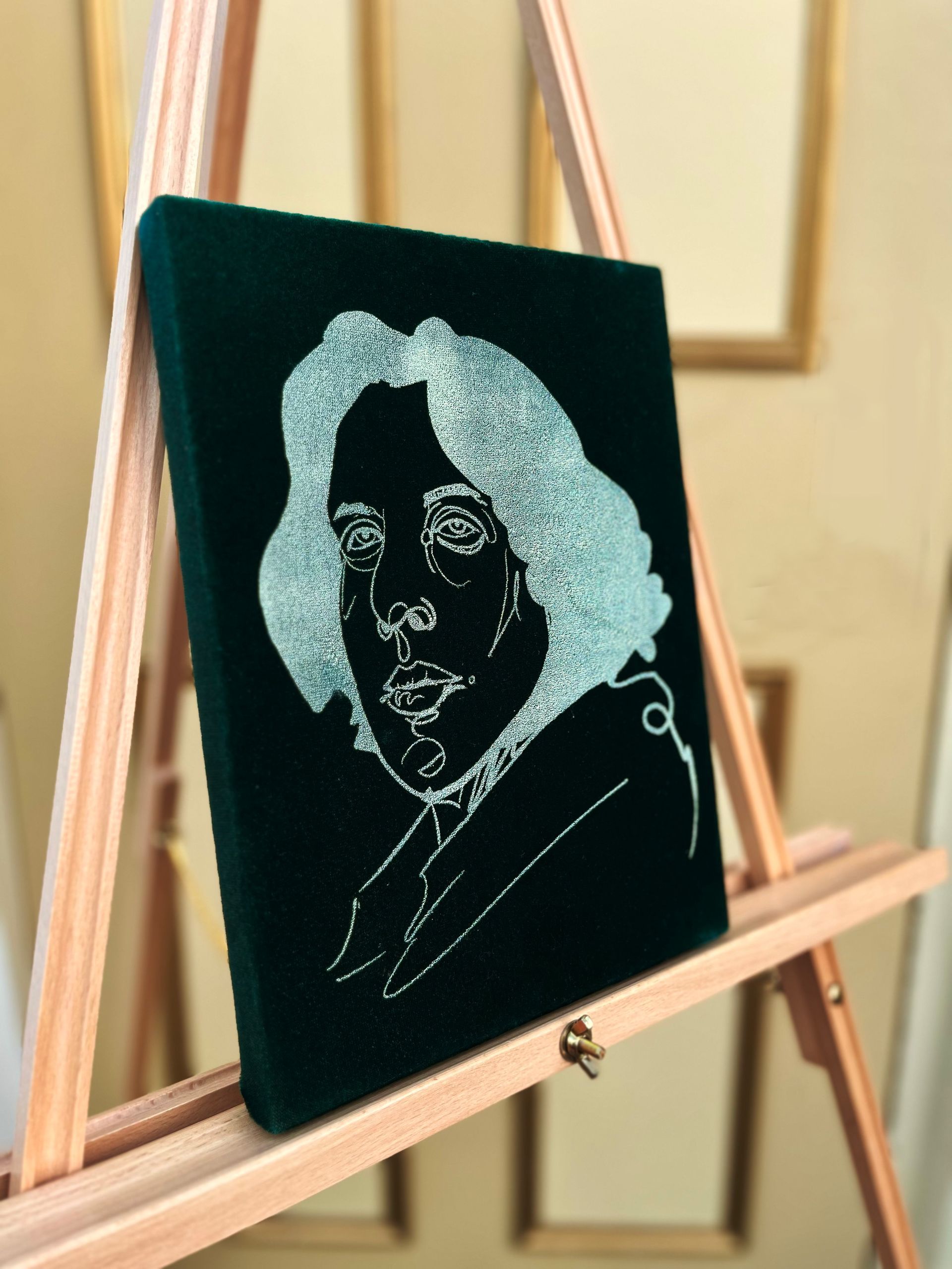 White line-art portrait on a black canvas displayed on a wooden easel.
