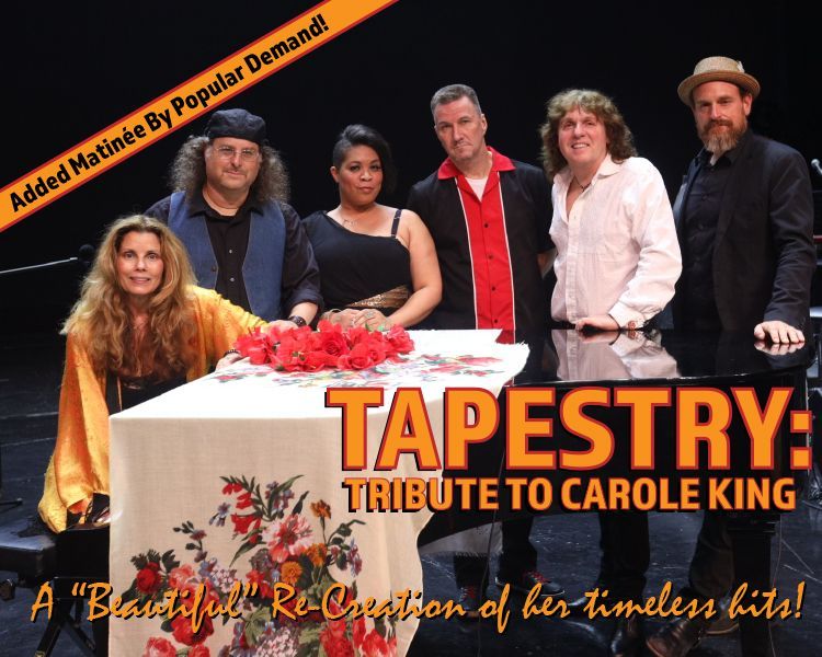 Cast of “Tapestry: Tribute to Carole King” posing on a dark stage with a piano and floral arrangement.
