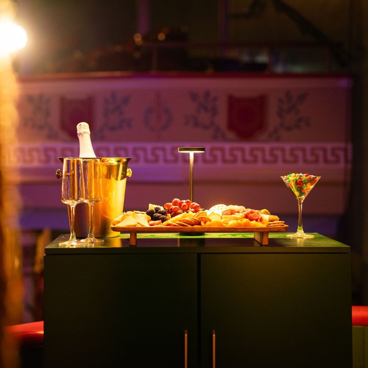 Cocktail and champagne bucket beside appetizers on a bar table under warm pink lighting