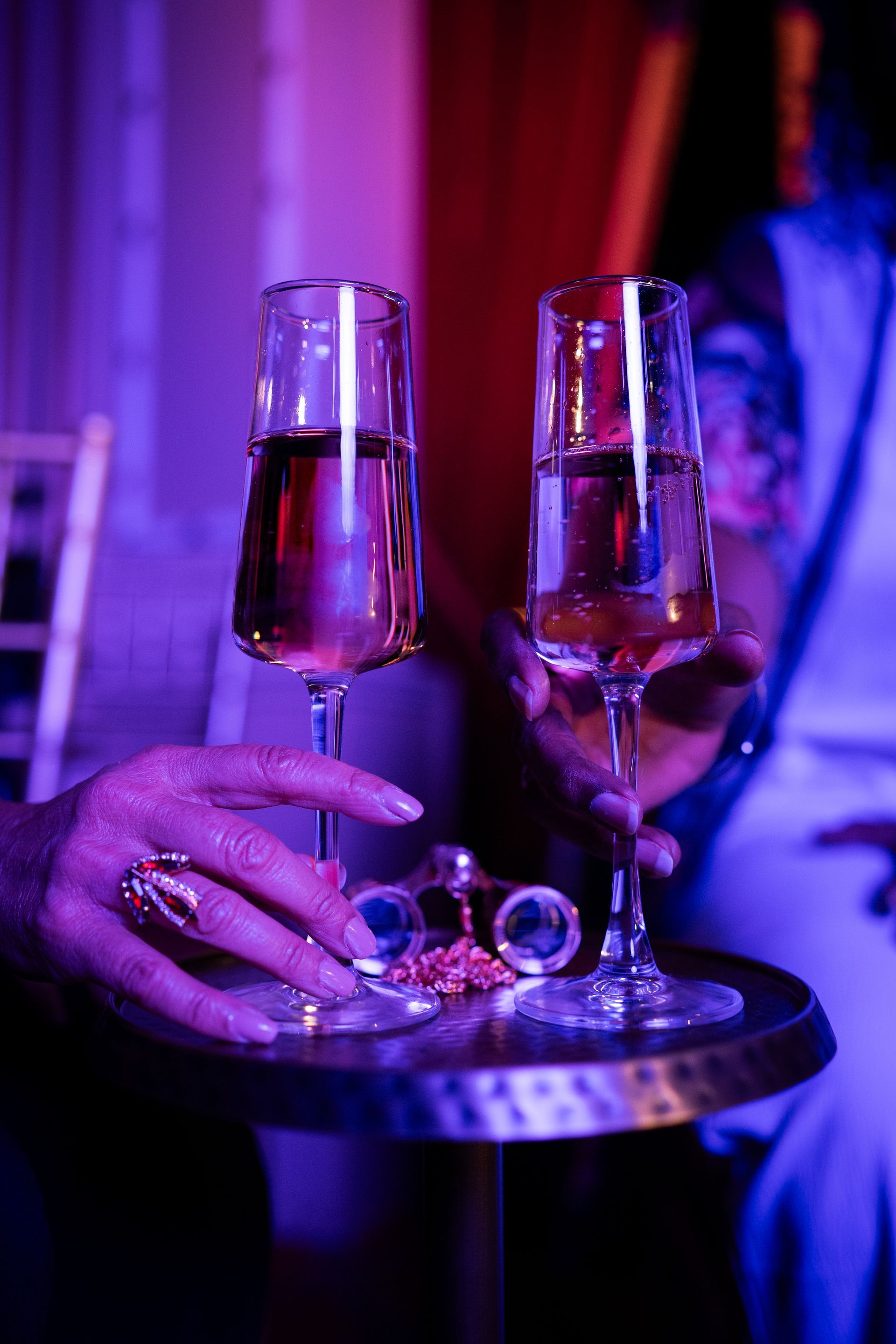 Two champagne flutes on a tray held by a hand in purple-blue nightclub lighting