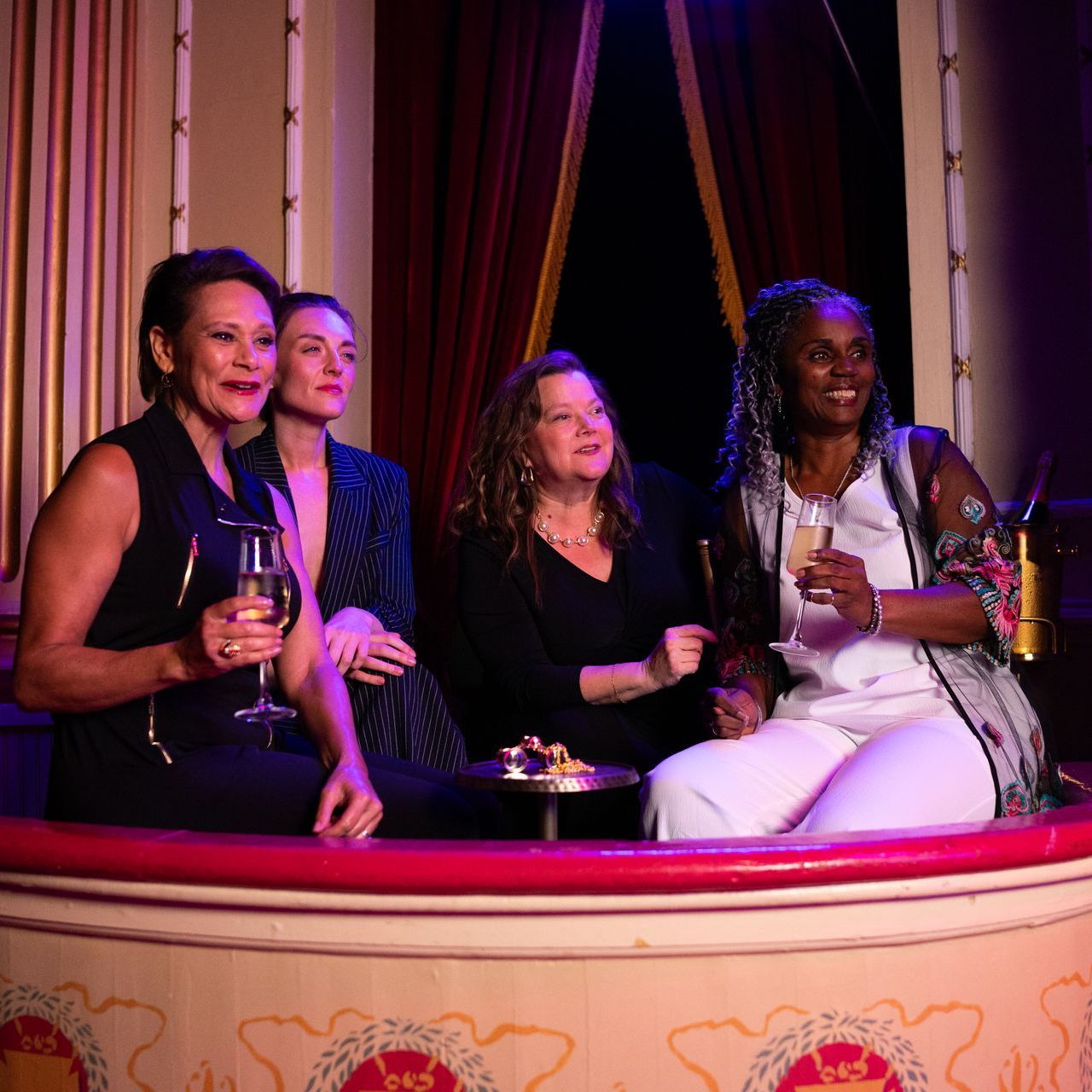 Four people seated in a decorative booth, holding drinks and smiling in a dimly lit lounge
