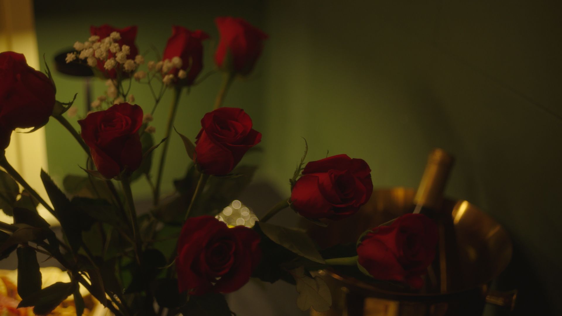 Red roses and small white flowers in a dim, warm-lit arrangement
