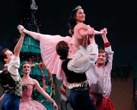 Theater dancers lift a smiling ballerina in a pink costume onstage.