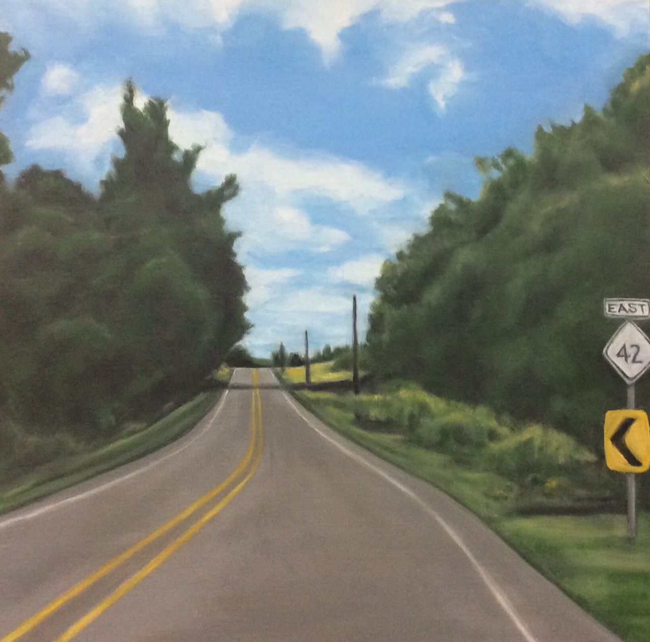 Rural road curving past trees, with yellow center lines and road signs ahead under a partly cloudy sky.