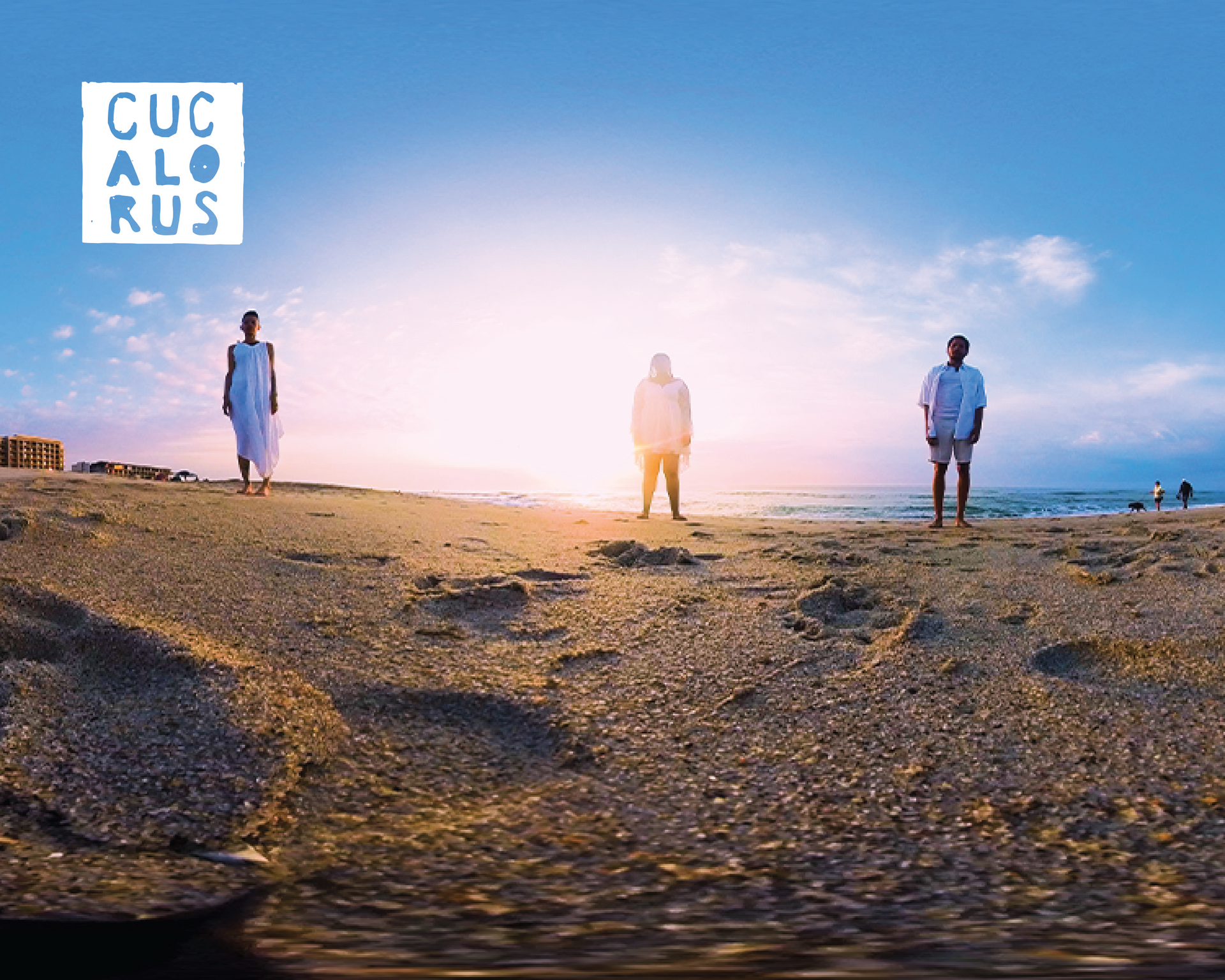 Three people standing on a rocky shore at sunset under a blue sky with a bright glow on the horizon.