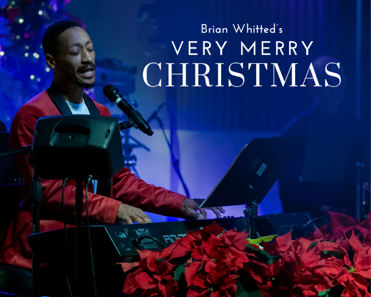 Brian Whitted singing at a microphone with laptop and poinsettias under 
