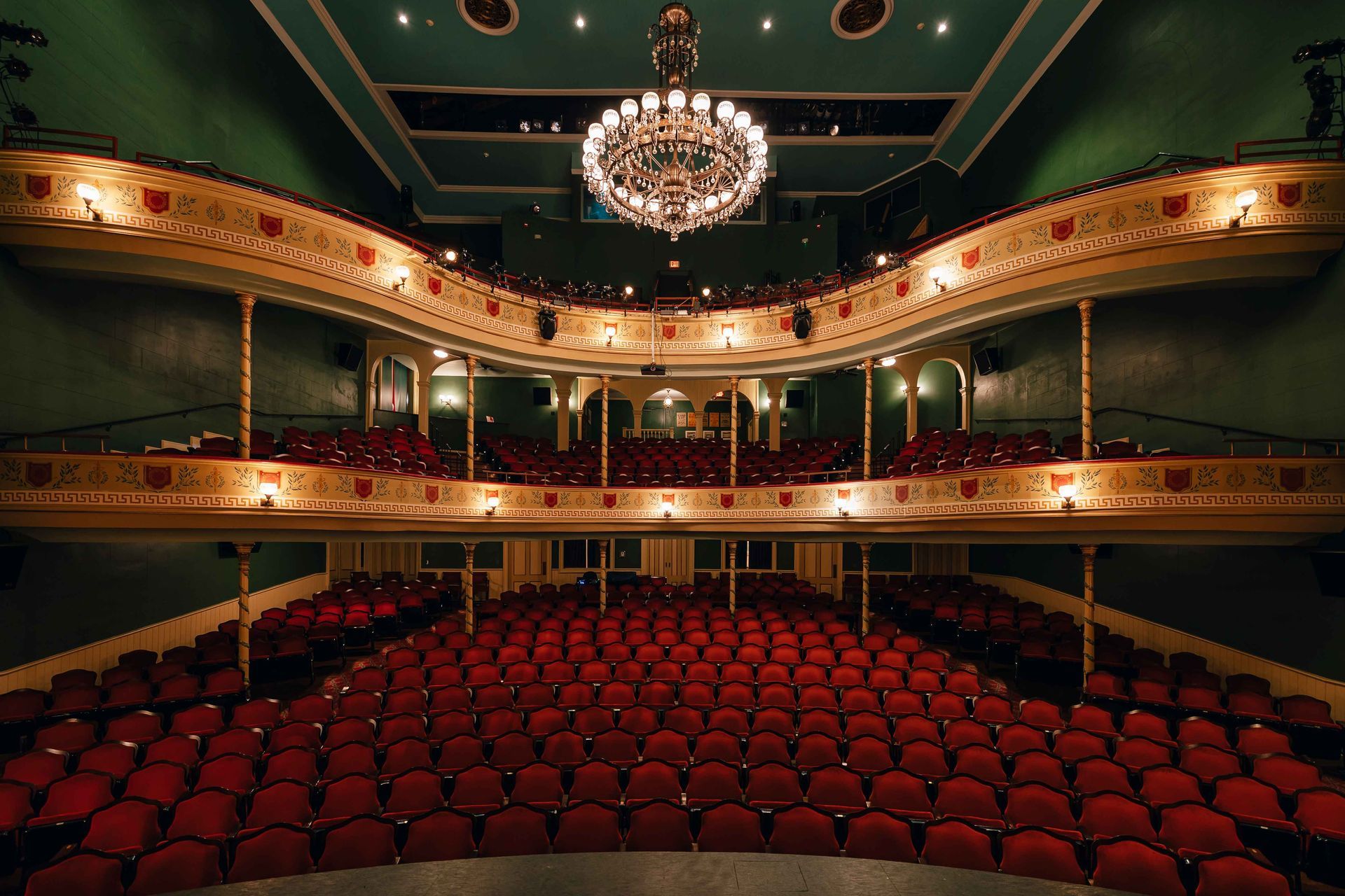 Ornate theater interior with red seats, gold balconies, and a large chandelier under a green ceiling