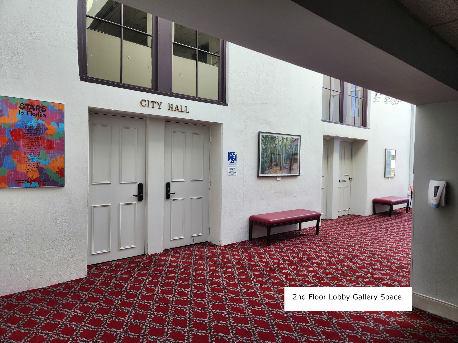 City Hall lobby with white doors, red patterned carpet, wall art, and benches.
