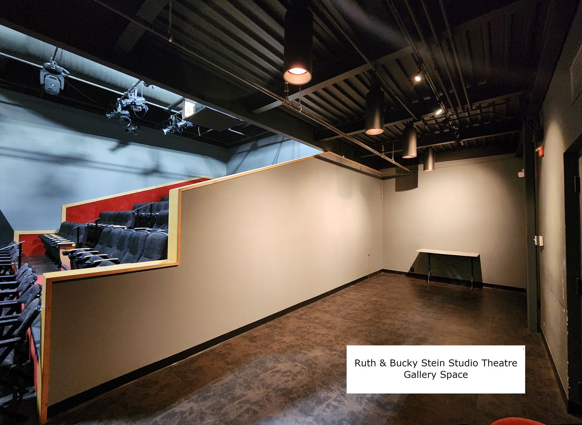Empty indoor theater seating area with black chairs, beige wall, and exposed ceiling lighting