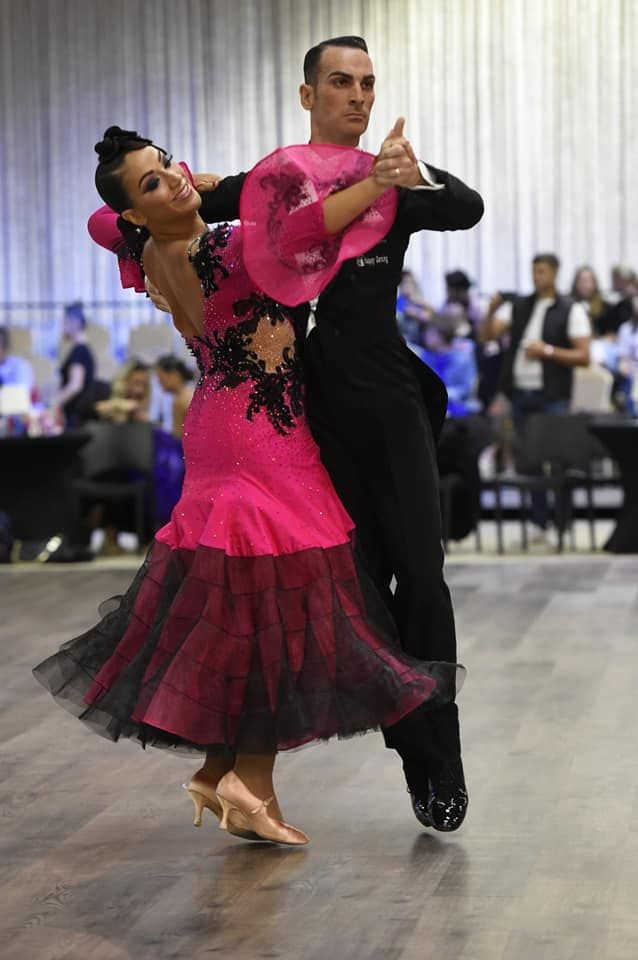 Una coppia in abiti da ballo formali si esibisce, la donna in abito rosa, l'uomo in abito nero, all'interno della sala da ballo.
