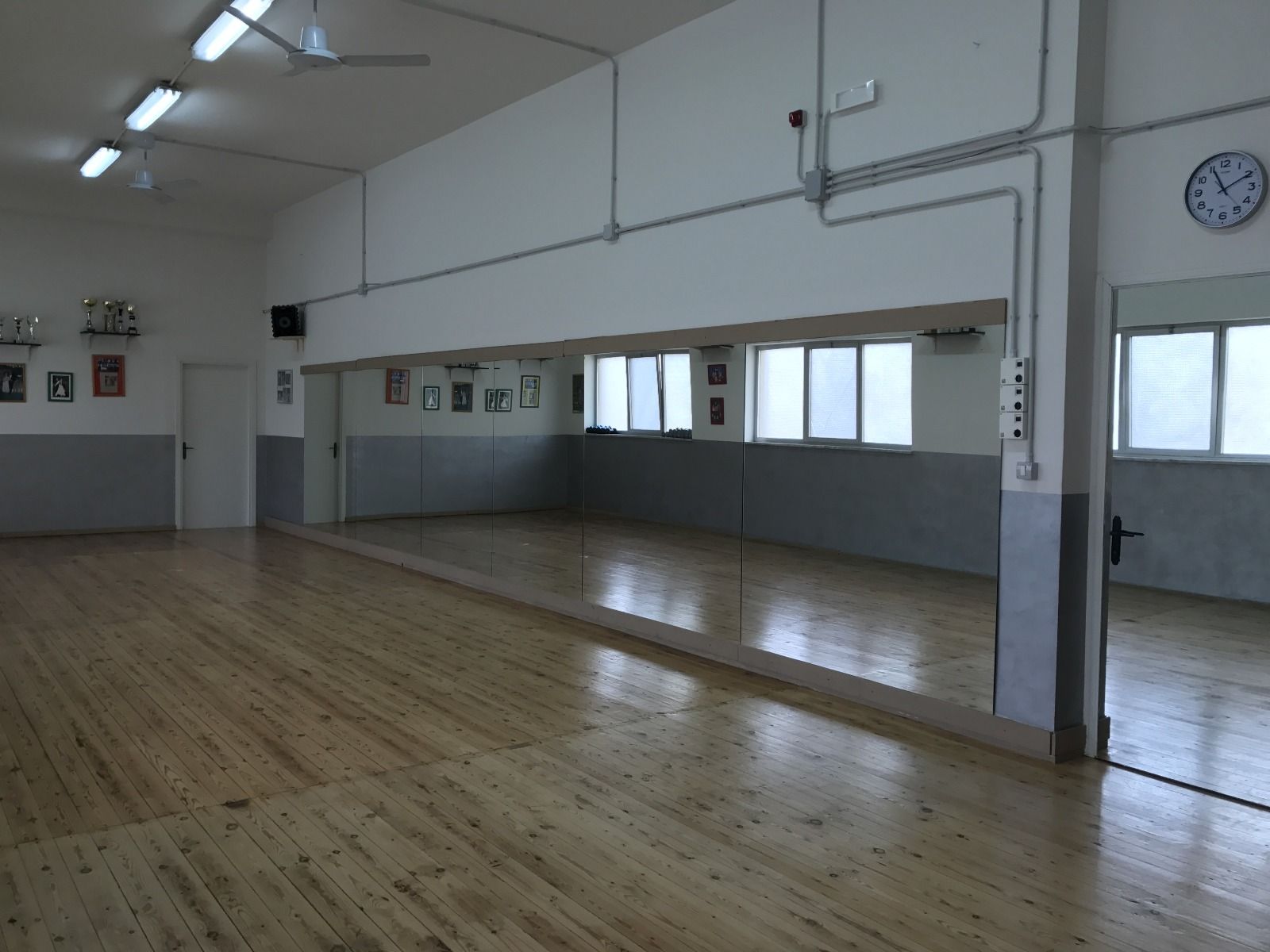 Studio di danza vuoto con parete a specchio, pavimento in legno e finestre.