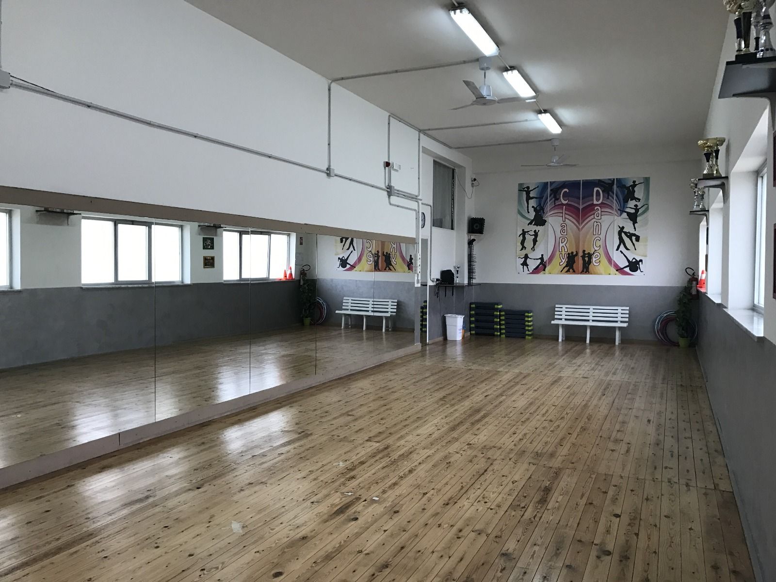 Studio di danza con parete a specchio, pavimento in legno e opere d'arte alle pareti.