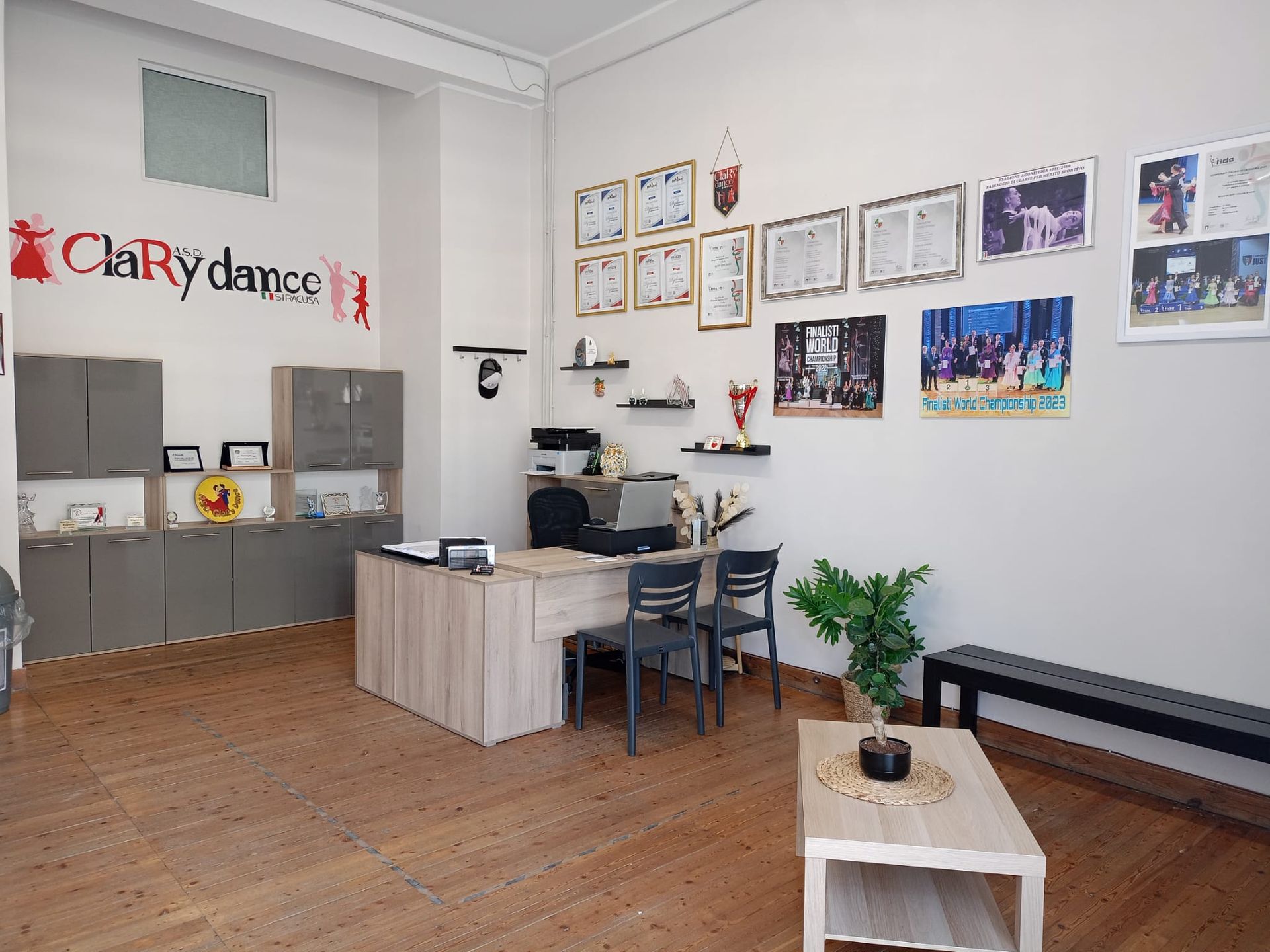 Ufficio studio di danza con scrivania, armadietti, premi e panca.