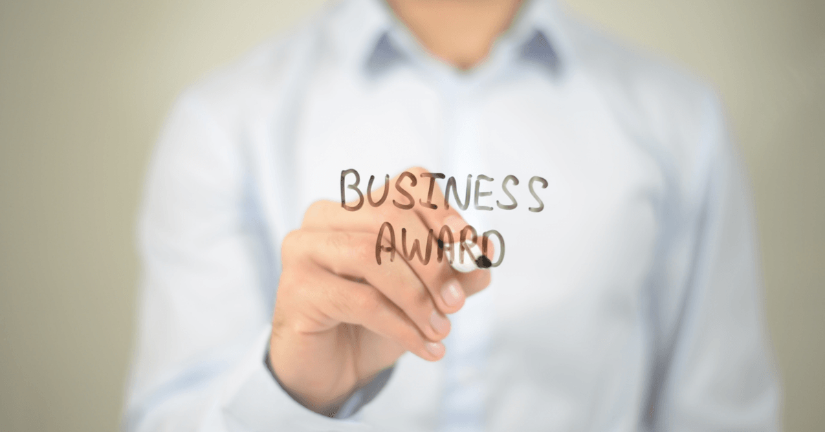 A person writing 'Business Award' with a whiteboard marker