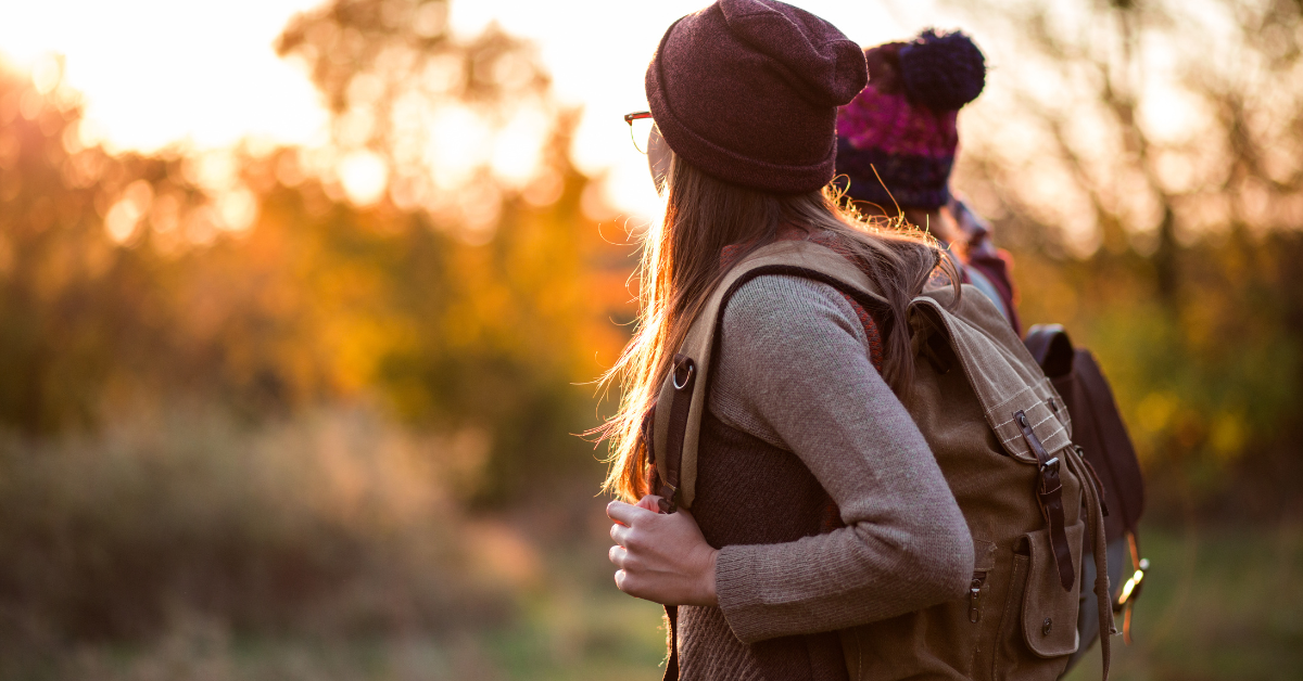 2 women with backpacks walking in the woods at sunset