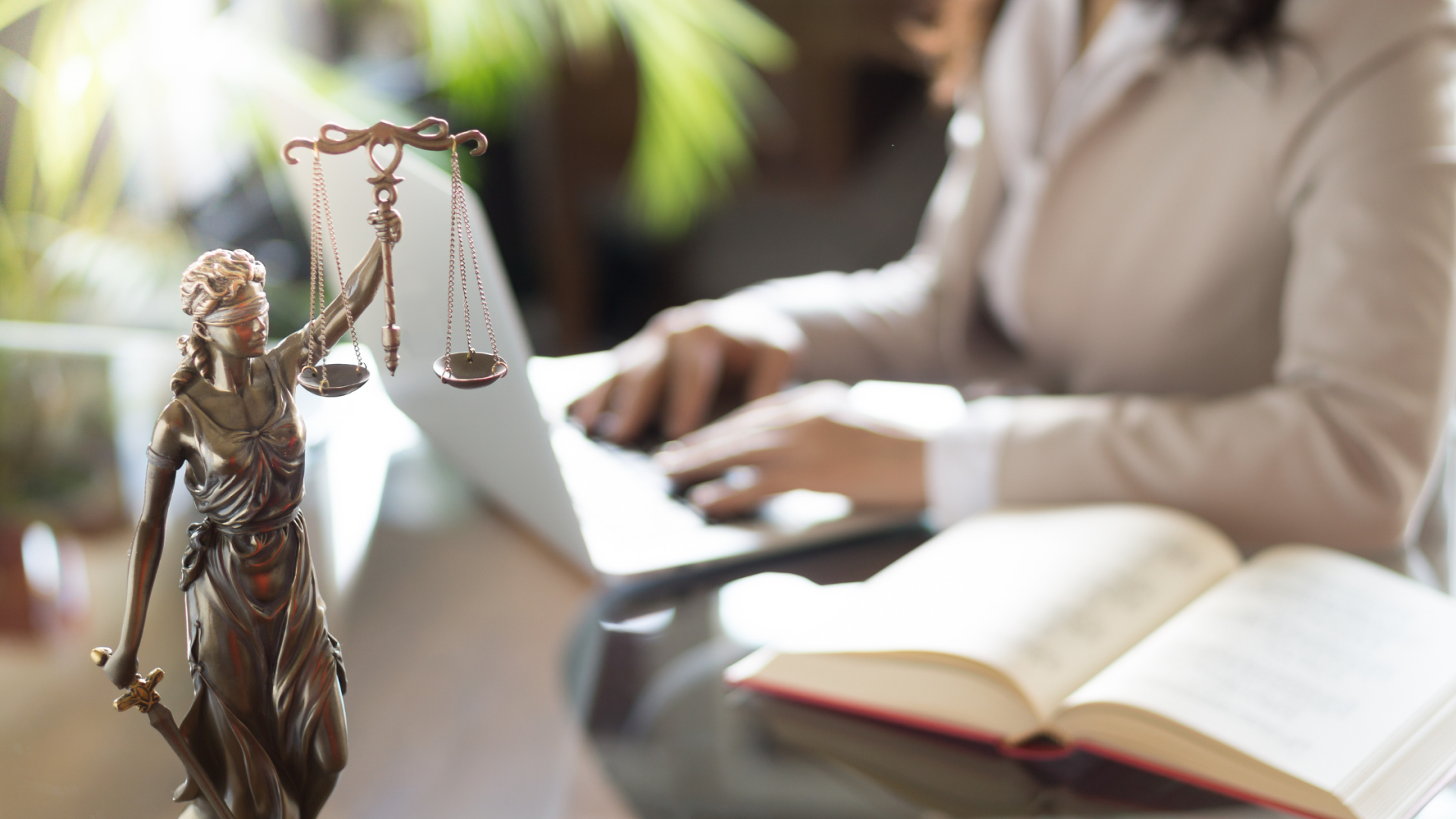 Person working on their laptop at a desk. A statute of the scales of justice is in the forefront