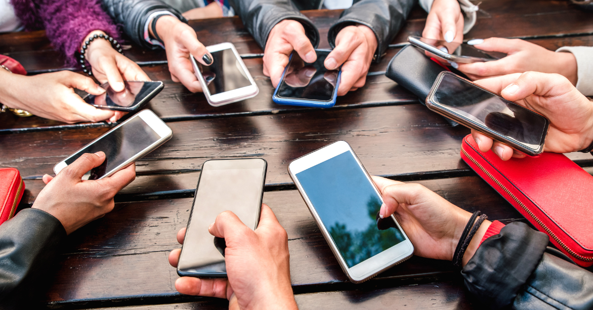 Group of people sitting at a table holding their cell phones in a circle