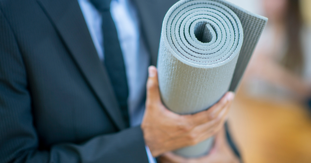 Man in suit carrying a rolled up yoga mat