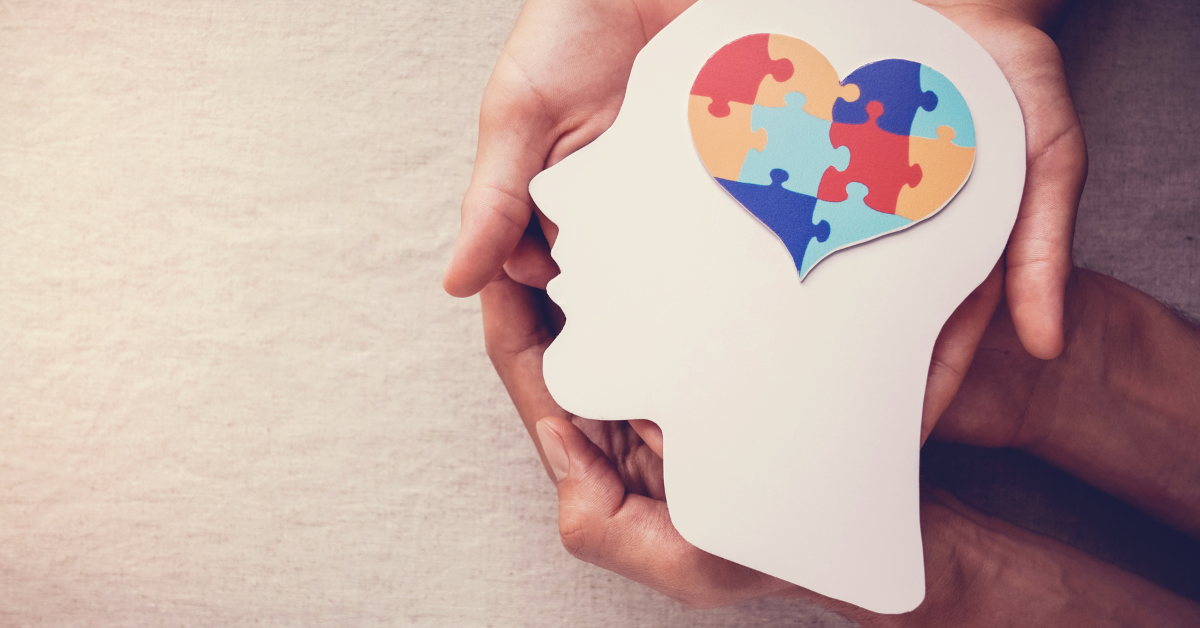 A person is holding a paper head with a heart made of puzzle pieces