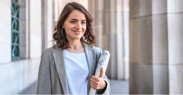 A woman is holding a newspaper and smiling while standing in front of a building.