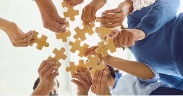 Hands connecting puzzle pieces in a teamwork circle on a bright white background