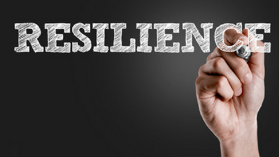 A person writing the word 'resilience' with a whiteboard marker