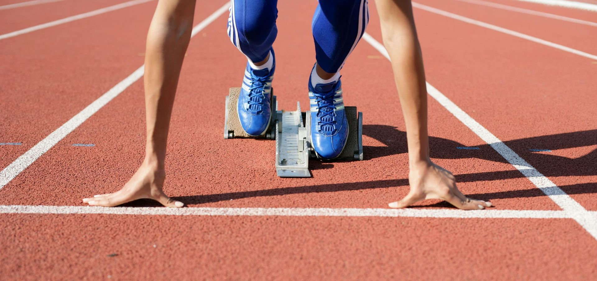 Sprinter in blue shoes crouching at the starting block on a race track