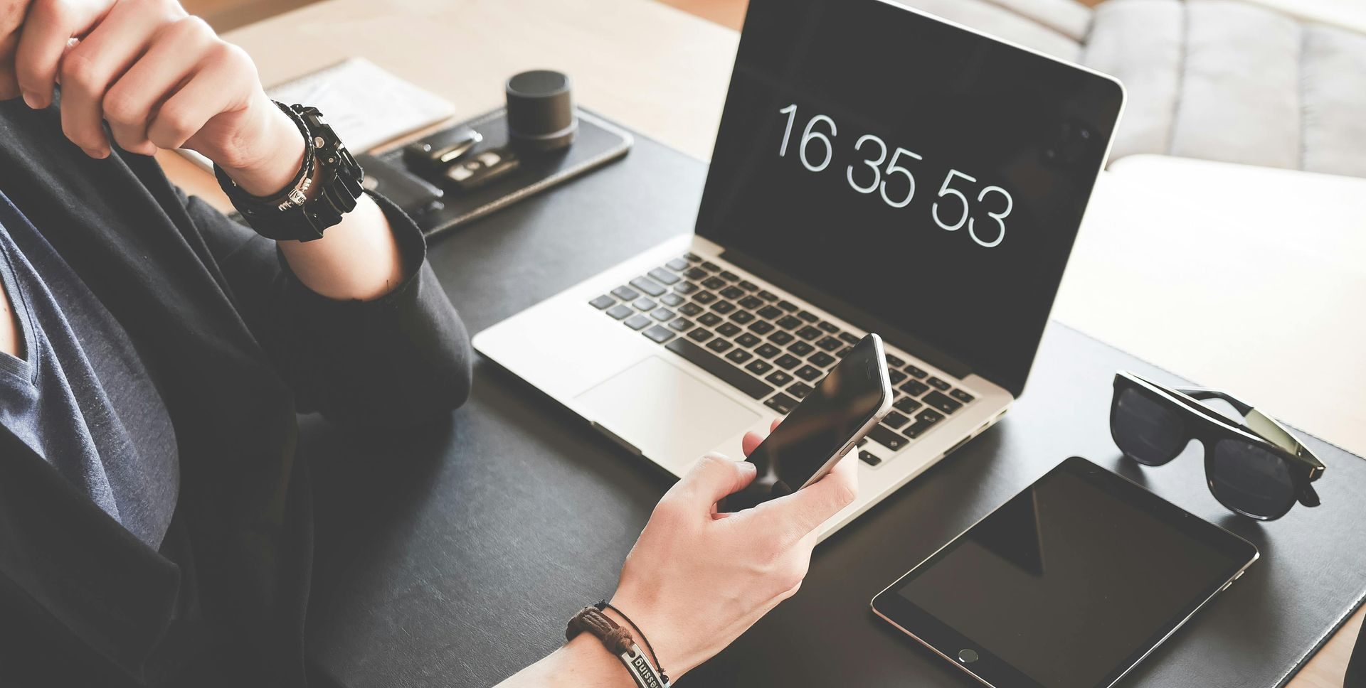 A person sitting at their desk using their mobile phone. Their laptop and tablet is on the desk