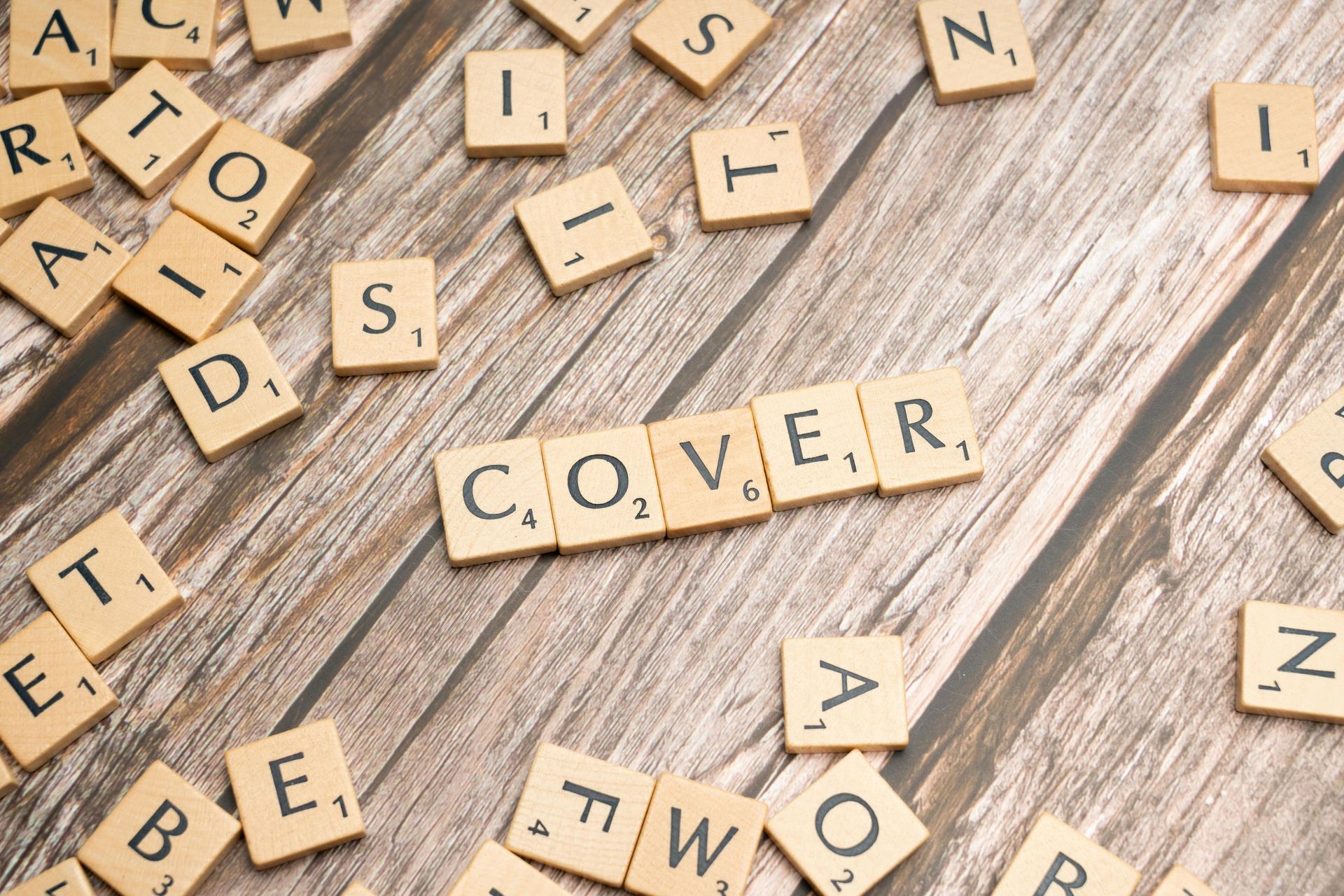 Scrabble tiles on a table. The word 'COVER' is spelt out