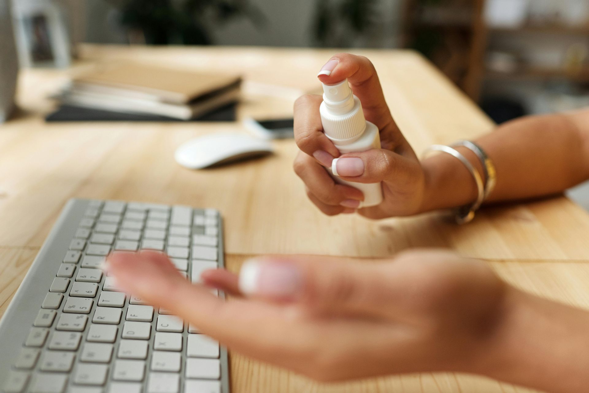 Worker sitting at their keyboard spaying hand sanitiser on their hands