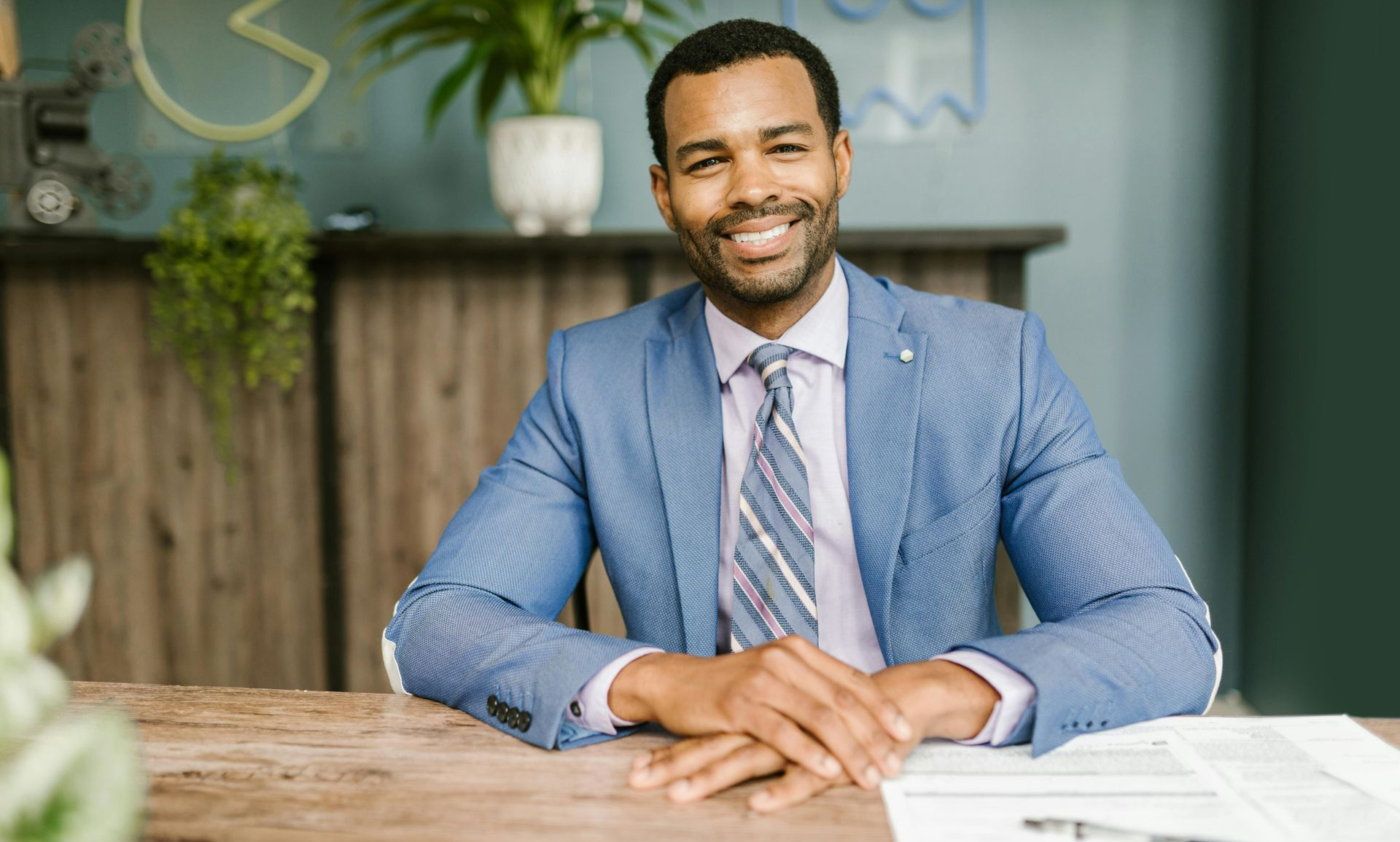 Man in blue suit with papers in front of him sitting at a desk and smiling