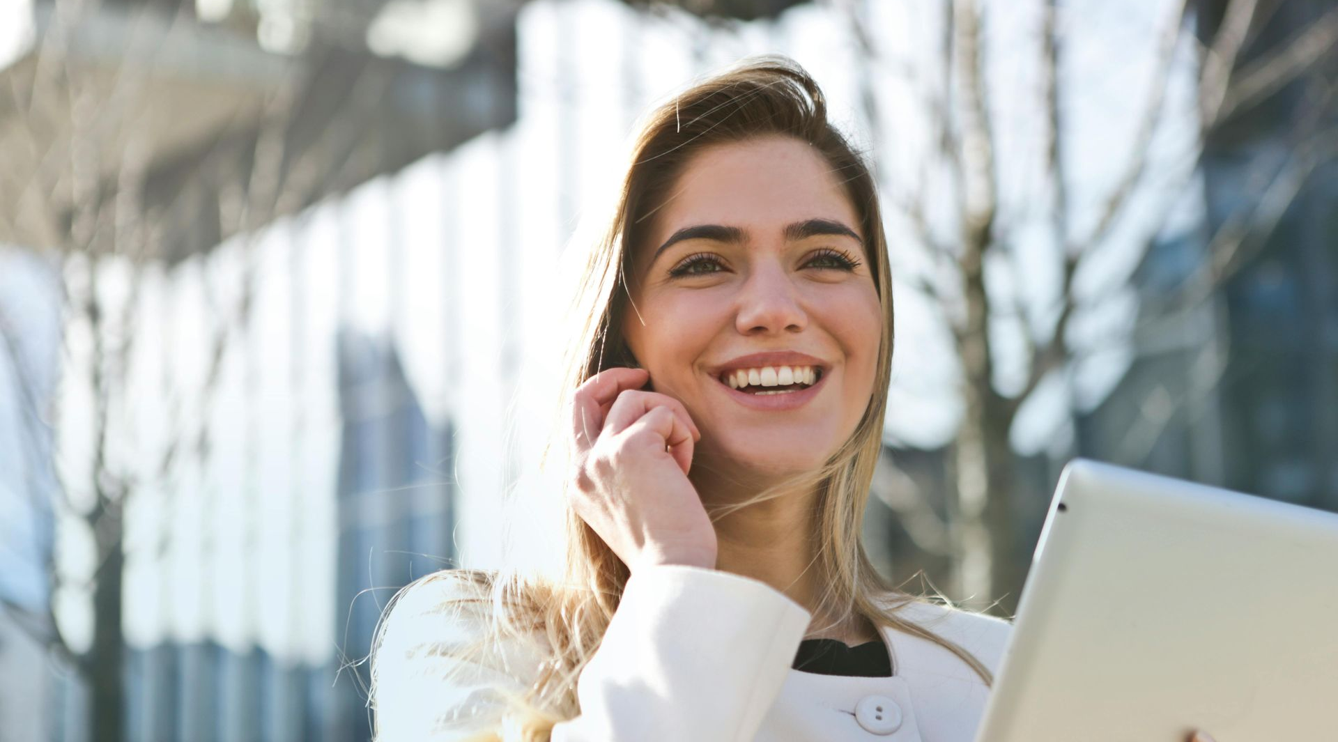Female smiling and holding a tablet while standing outside an office building