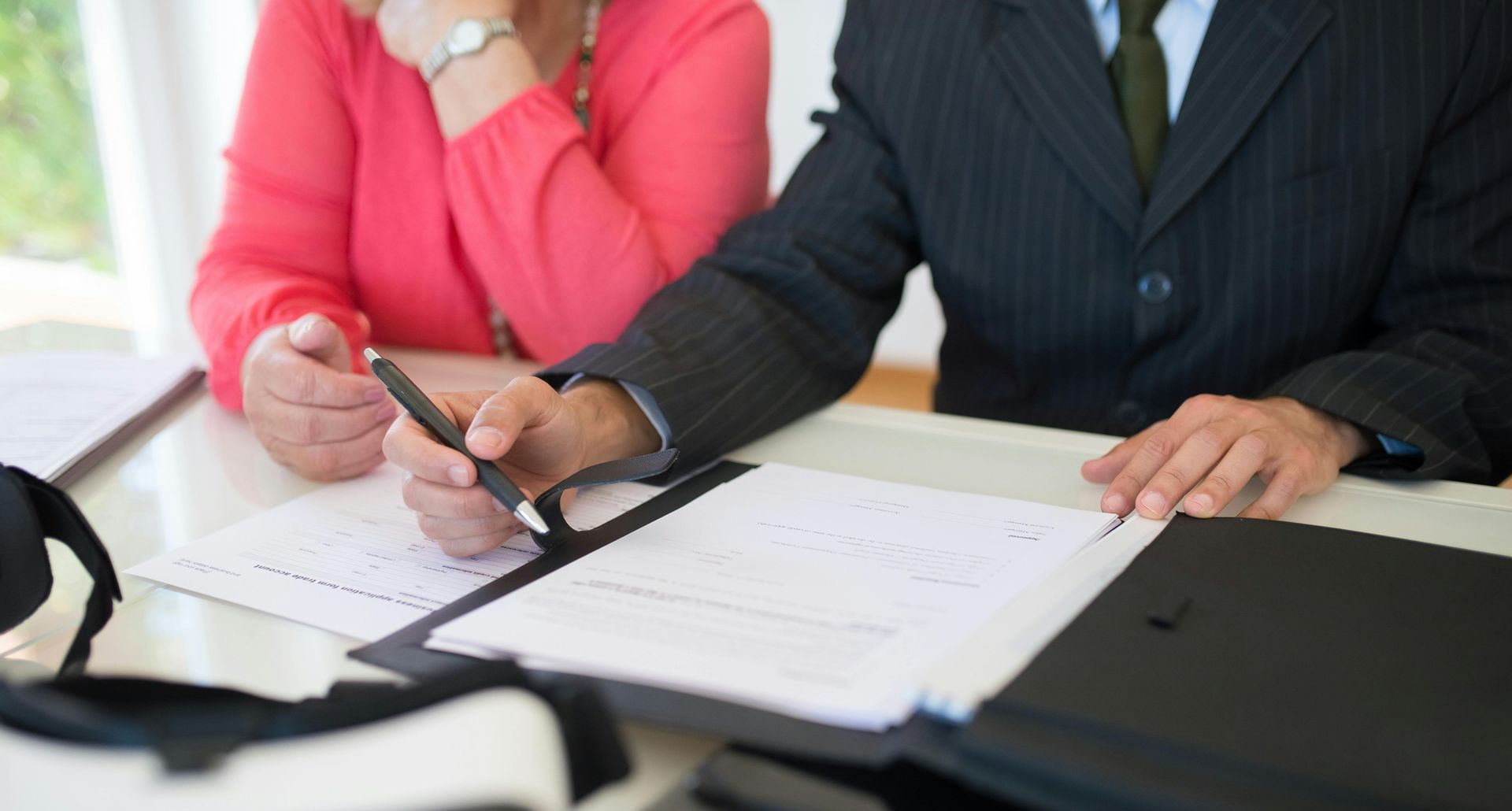 Two people reviewing documents at a desk, one pointing at paperwork with a pen.