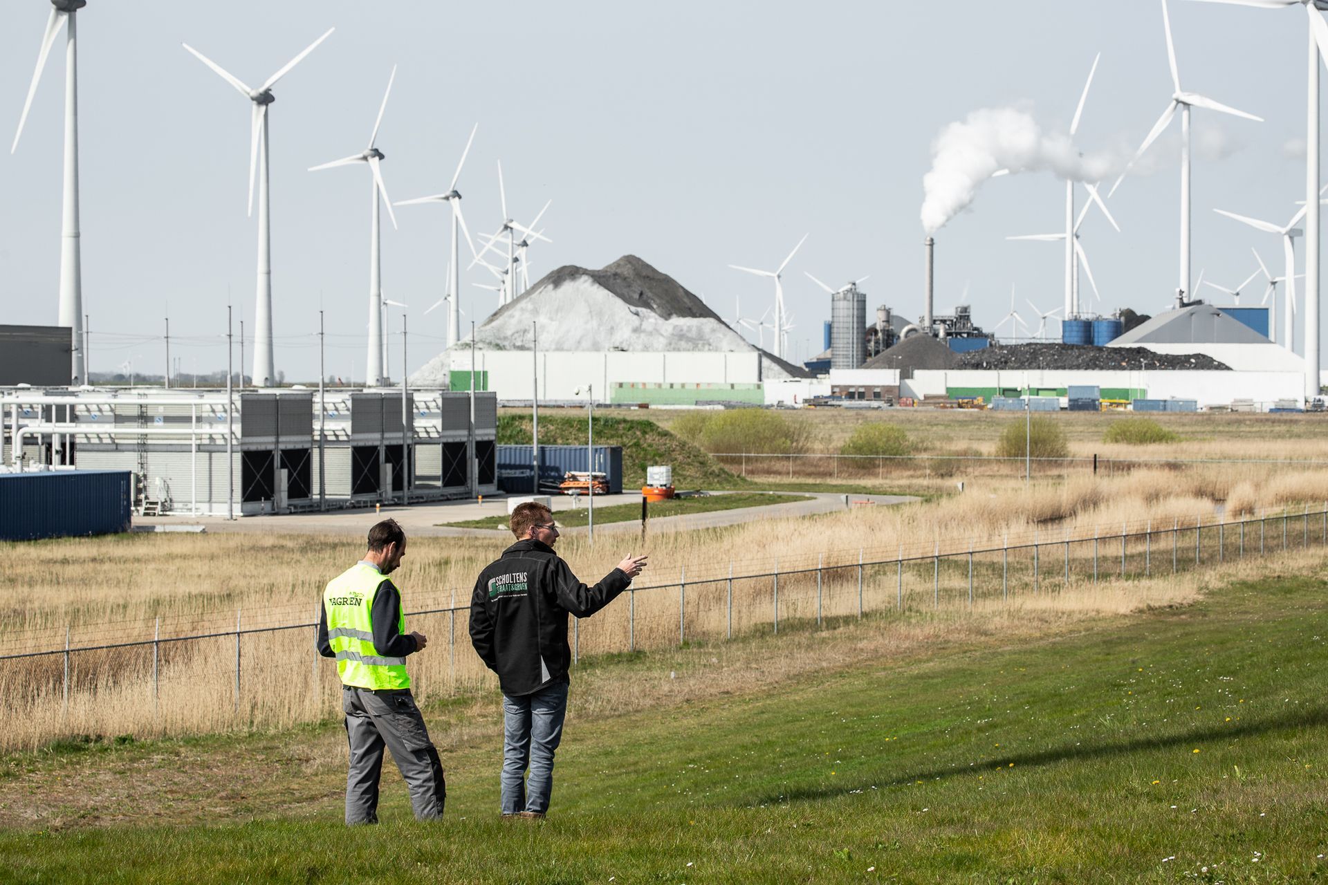 Twee mannen staan ​​in een veld met windturbines op de achtergrond.