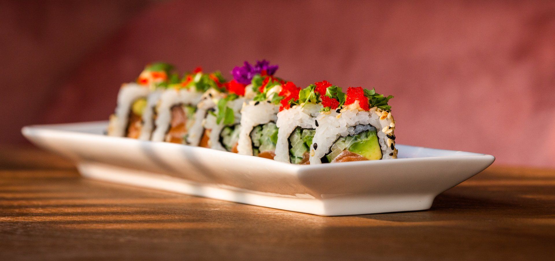 Een wit bord met sushirollen op een houten tafel.