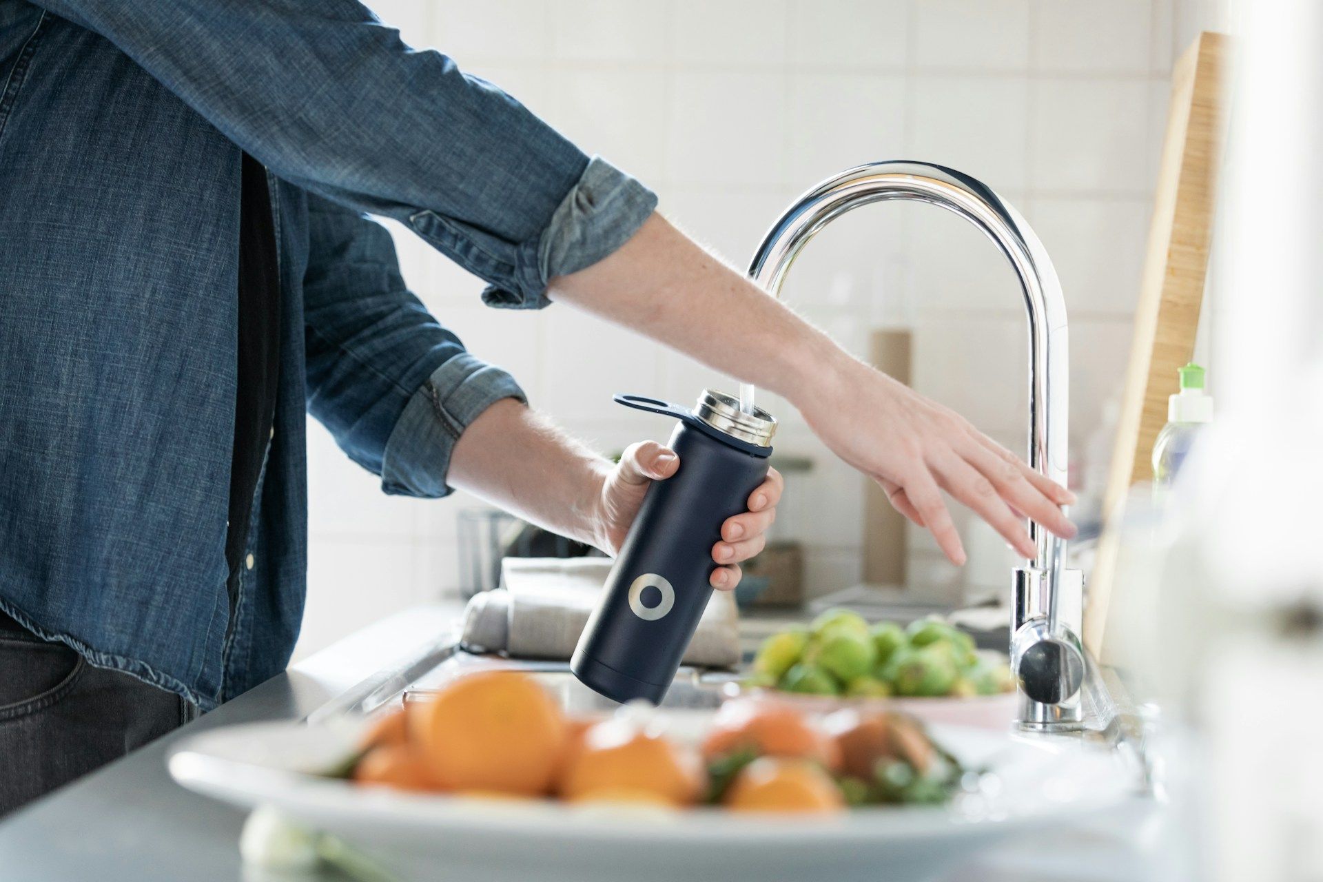 Person washing vegetables at a kitchen sink while holding a bottle under the faucet