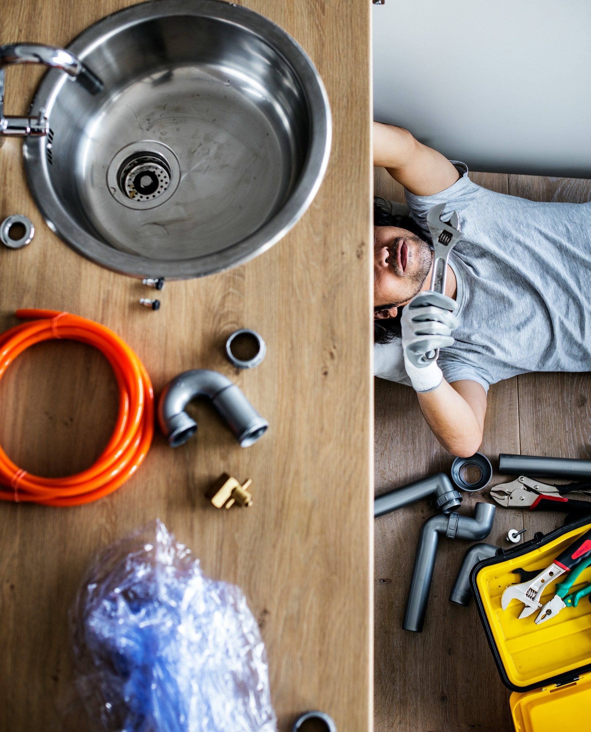 Plumber working under a kitchen sink using a drain cleaning machine.