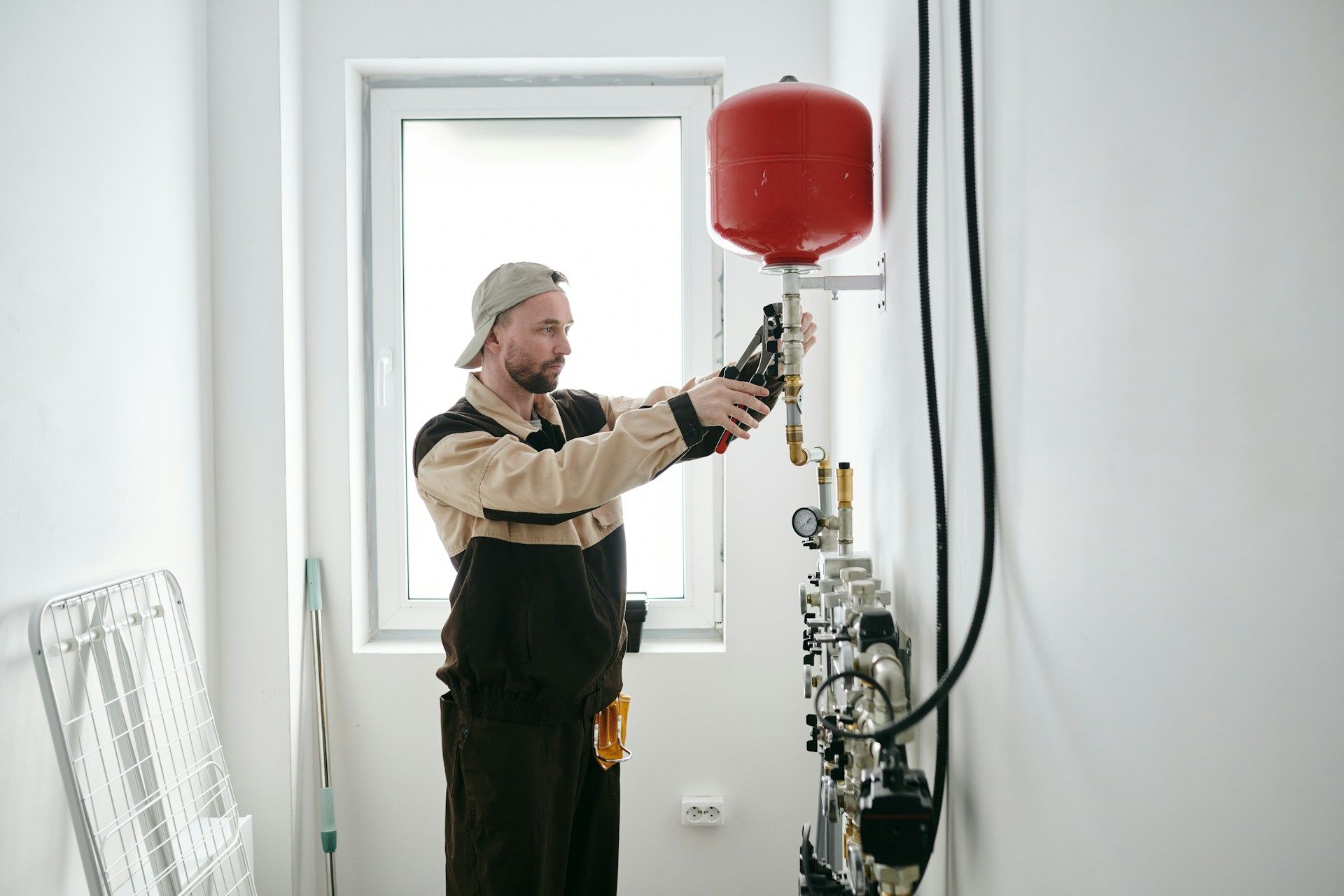 Technician adjusting a red pressure tank and equipment beside a window in a bright room