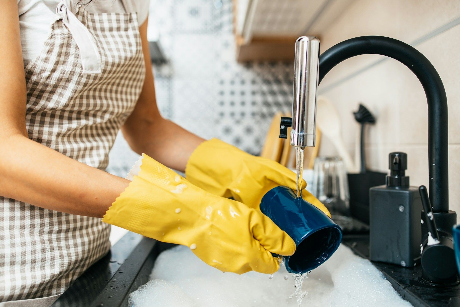 Person in yellow gloves washing a mug at a kitchen sink with running water